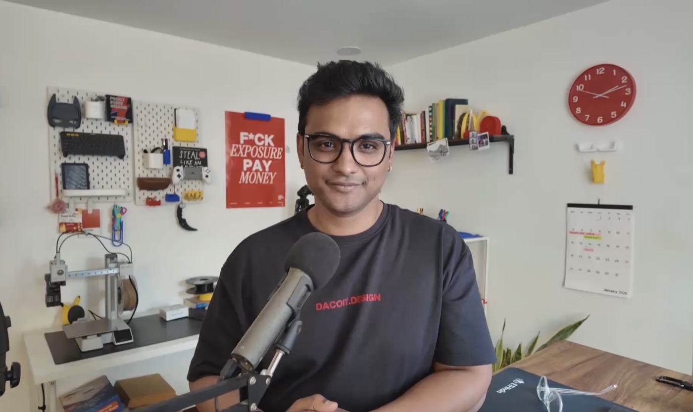 Rahul at his desk in the build room, mic in front, pegboard and 3D printer behind